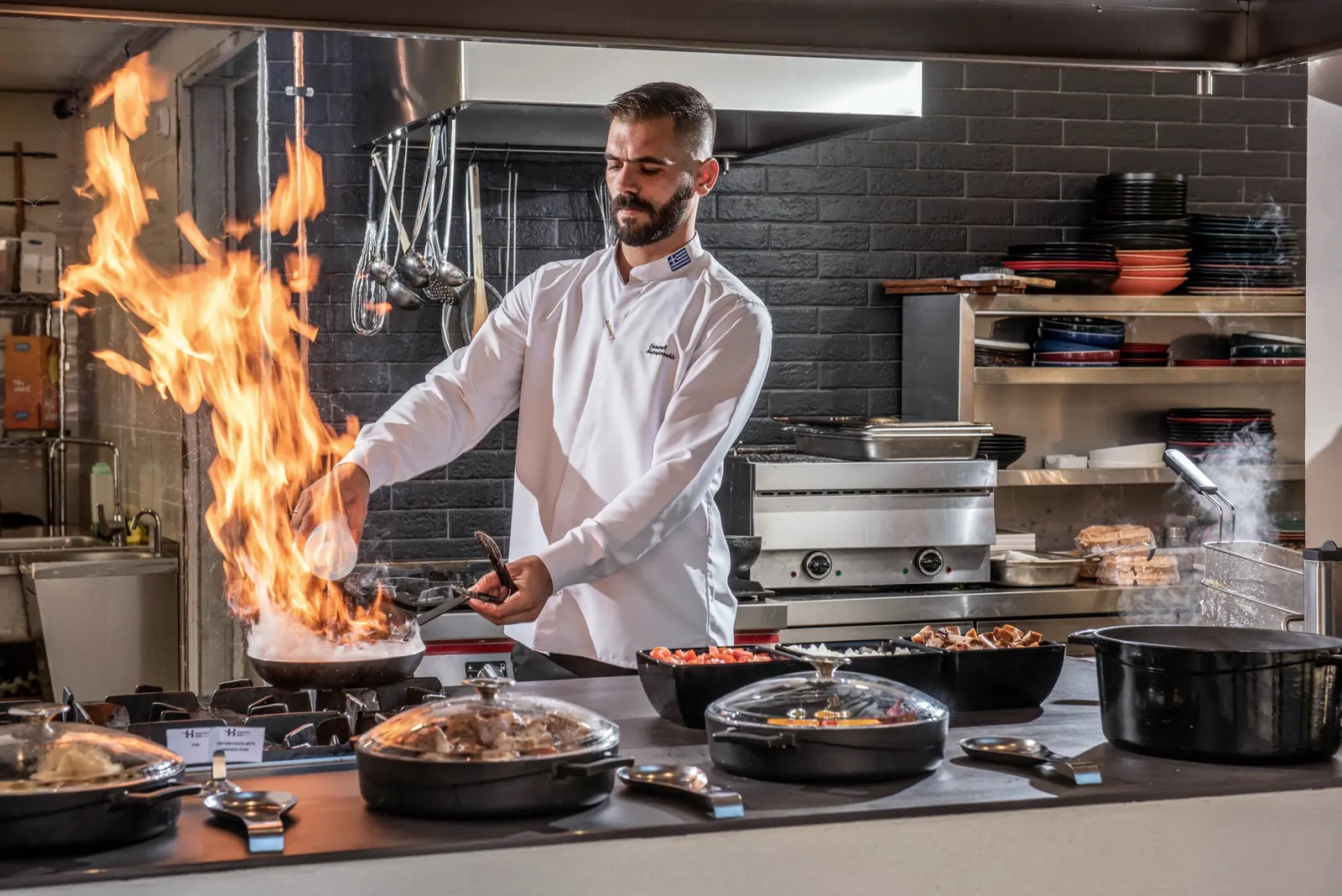 Chef flambéing in an open kitchen with cast-iron pans
