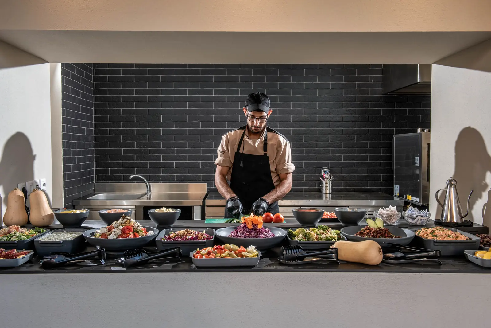 Cook preparing salads behind a buffet counter with grey ceramics