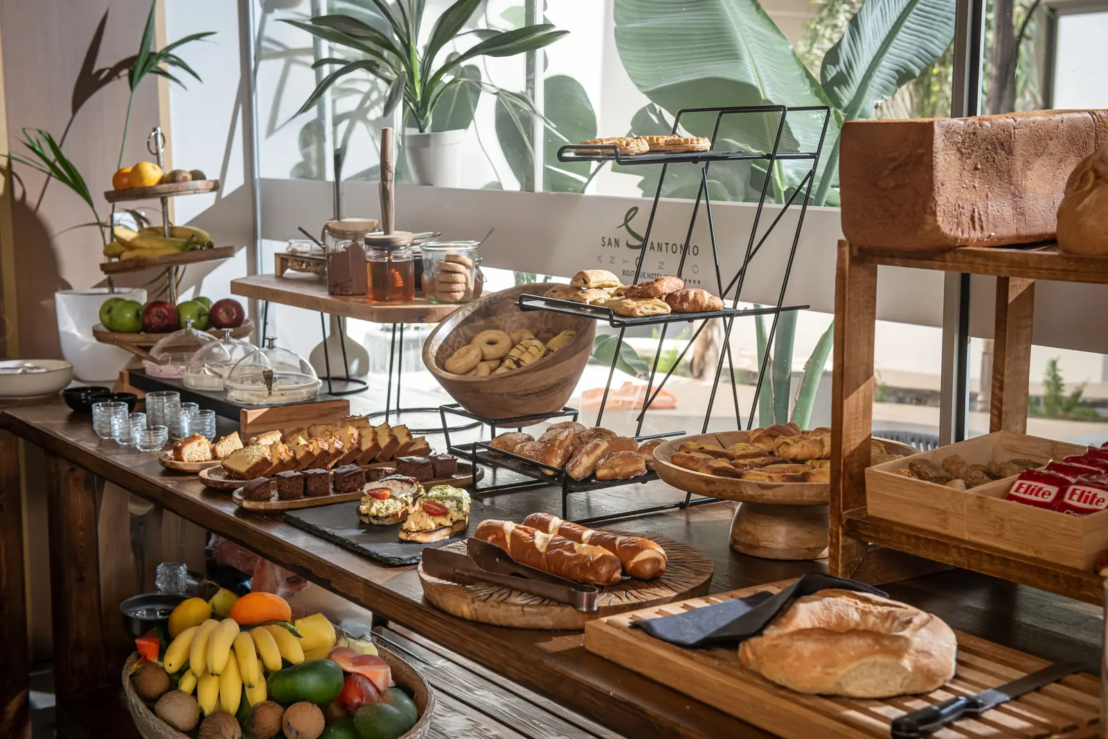 Pastry, cake and fruit buffet on wood and metal stands with plants behind